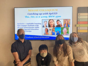 Photograph of Dr. Dor Abrahamson, Rachel Chen, Sofia Tancredi, and Dr. Christina Krause standing in front of a poster for a Special Education Embodied Design talk at the Berkeley SESAME Colloquium. They are all wearing masks and kneeling down so that the digital flyer is visible. The flyer show pictures of eight speakers including the four in the picture and includes the title "Catching Up With SpEED" and the subtitle "inclusive and equitable learning that engages students with diverse sensorimotor skills through Special Education Embodied Design". 